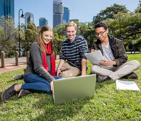 Three individuals sitting on the lawn looking at a laptop